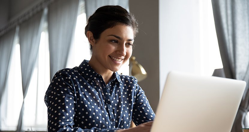 A woman entrepreneur smiling while working on her laptop at a desk